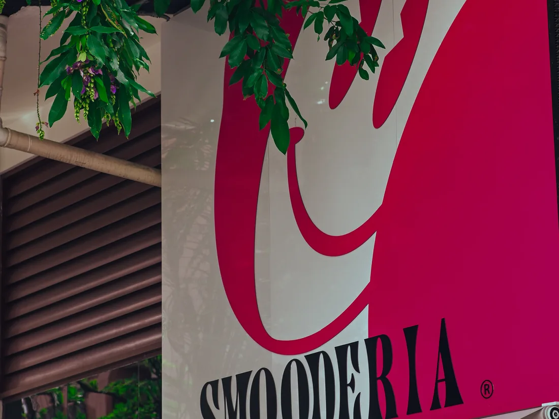 Placa da Smooderia na fachada, letreiro branco sobre fundo magenta